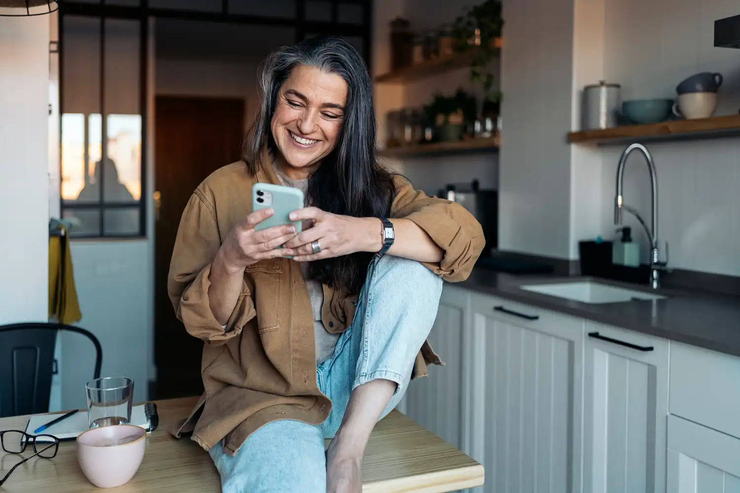 Woman casually sitting on table smiling while looking at her phone