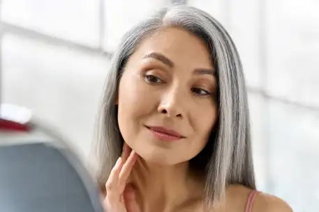 woman subtly smirking while looking at her face in a bathroom mirror